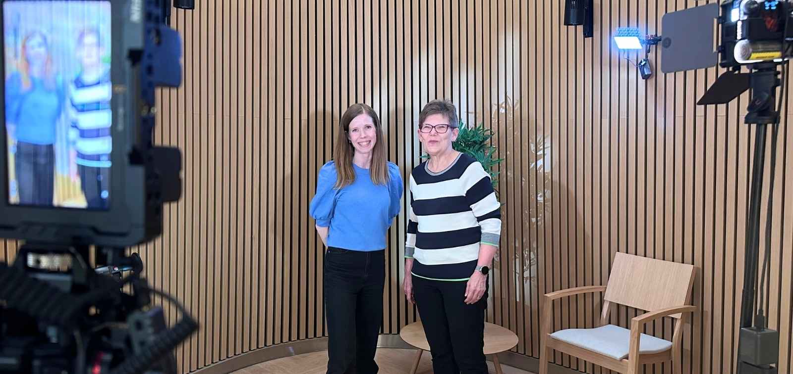 Anna-Elina Rahikainen and Dr. Päivi Lähteenmäki smiling on a filming set with cameras and studio lights during a session for the e-QuoL project at Siltasairaala (Bridge Hospital), HUS Helsinki University Hospital.